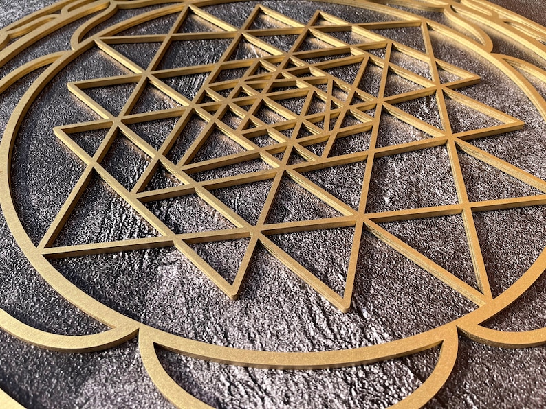 May include: A gold geometric design with a circular frame on a dark gray background. The design is made up of overlapping triangles.