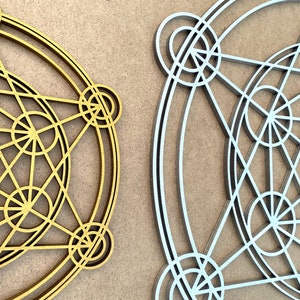 May include: Two geometric designs, one in gold and one in silver, are displayed on a brown background. Both designs are circular and feature intricate patterns of overlapping circles and lines.