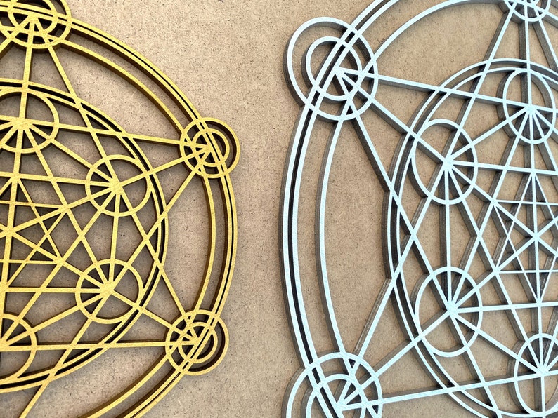 May include: Two geometric designs, one in gold and one in silver, are displayed on a brown background. Both designs are circular and feature intricate patterns of overlapping circles and lines.