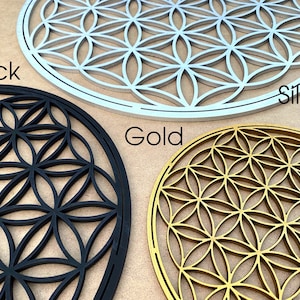May include: Three wooden wall decor pieces in the shape of a flower of life pattern. The pieces are in black, silver, and gold.