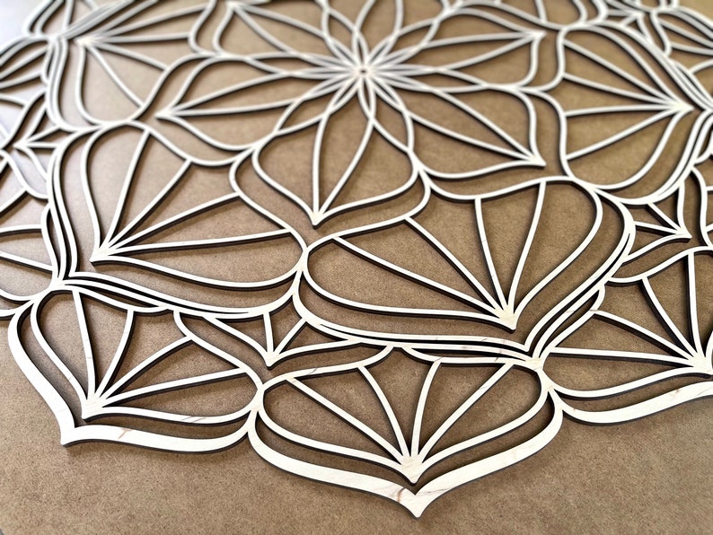 Op de afbeelding: Een witte houten mandala met een geometrisch ontwerp. De mandala is gemaakt van meerdere lagen hout die zijn uitgesneden om een ingewikkeld patroon te cre&euml;ren.