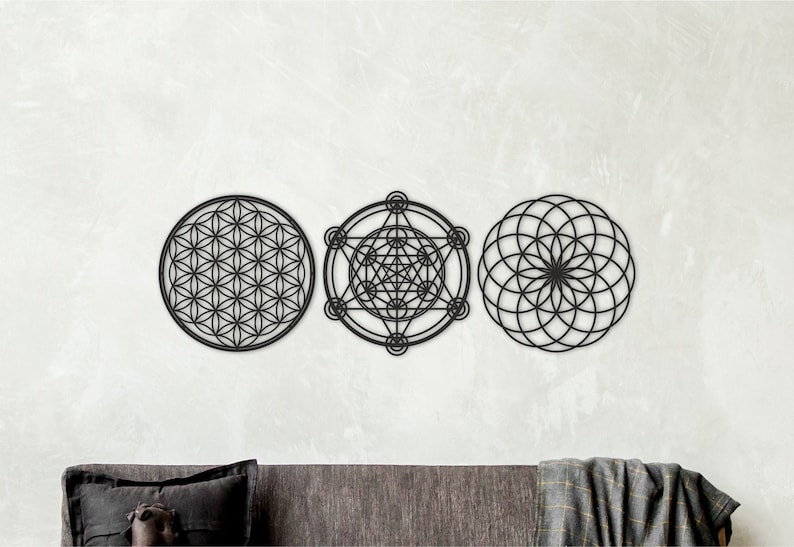 May include: Three black metal wall decor pieces featuring geometric designs. The designs are a flower of life, a metatron's cube, and a seed of life.