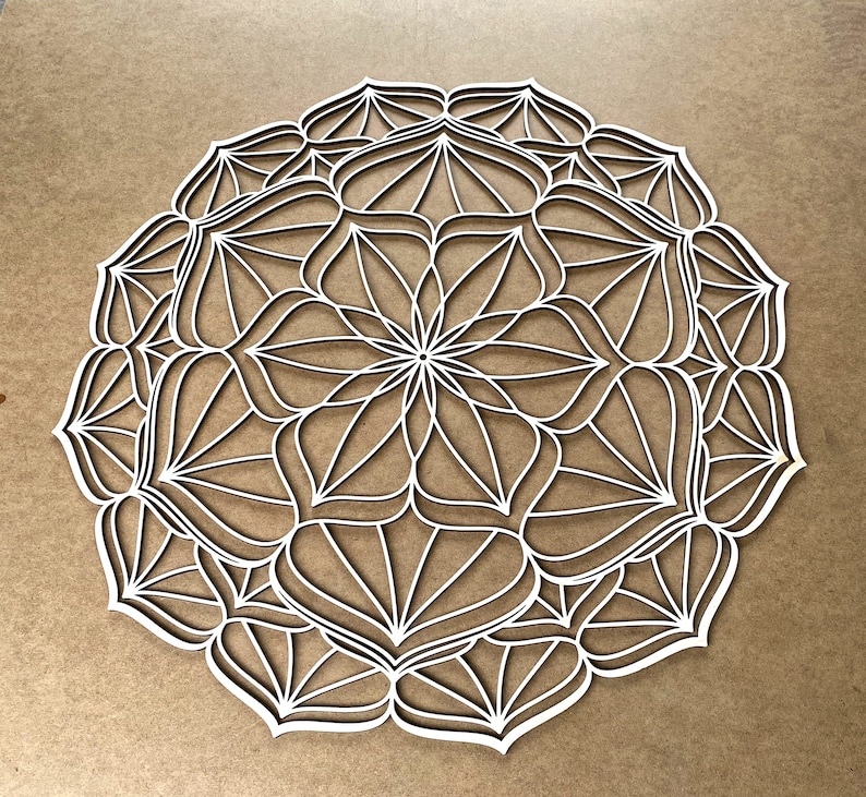Op de afbeelding: Witte, ingewikkelde mandala-ontwerp met een cirkelvormig patroon van overlappende vormen en lijnen. Het ontwerp is symmetrisch en heeft een delicate, ingewikkelde uitstraling.