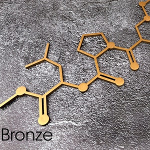 K&ouml;nnte beinhalten: Eine goldfarbene Metall-Molek&uuml;lstruktur auf einem grauen, strukturierten Hintergrund. Das Wort "Bronze" steht unter der Struktur.