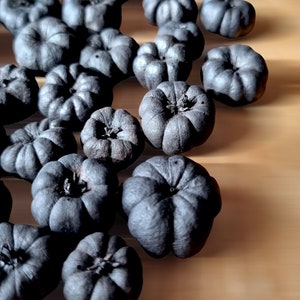 May include: A group of small, dark grey pumpkins arranged on a light brown wooden surface. The pumpkins are all different sizes and shapes, and some have a slightly textured surface.