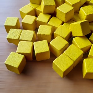 Puede incluir: Un montón de cubos de madera de color amarillo brillante. Los cubos están esparcidos sobre una superficie de madera.