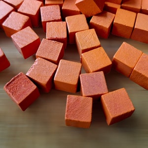 May include: A pile of small, orange wooden cubes. The cubes are arranged in a random pattern, with some cubes stacked on top of others.