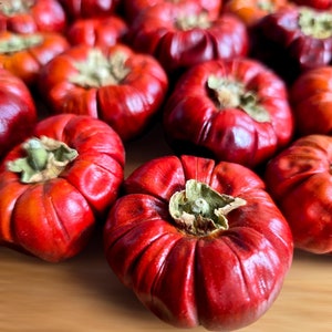 May include: A group of ripe, red persimmons, displaying a ribbed texture and green calyxes. The fruits are presented on a light brown surface, emphasizing their deep colour and natural shape. The image focuses on the fresh produce.