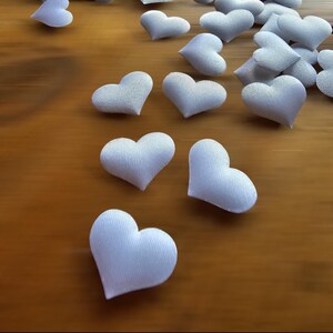 May include: A scattering of white felt hearts on a wooden surface. The hearts are arranged in a random pattern, with some hearts overlapping others. The hearts are all the same size and shape.