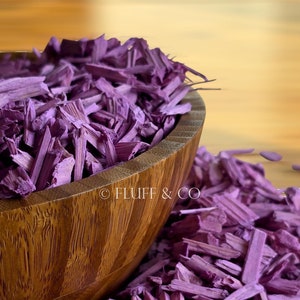 Puede incluir: Un cuenco de madera lleno de virutas de madera de color púrpura. El cuenco está sentado sobre una pila de virutas de madera de color púrpura.