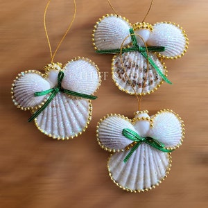 May include: Three white seashell Christmas ornaments shaped like angels with gold trim and green ribbon bows.