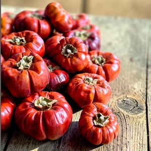 May include: A collection of small, round, bright red fruits with a ribbed texture and a dried brown calyx at the top. These fruits are clustered together, displaying a glossy, firm skin and a vibrant, deep red colour throughout the entire group.