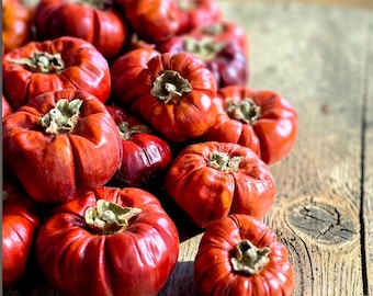 May include: A collection of small, round, bright red fruits with a ribbed texture and a dried brown calyx at the top. These fruits are clustered together, displaying a glossy, firm skin and a vibrant, deep red color throughout the entire group.