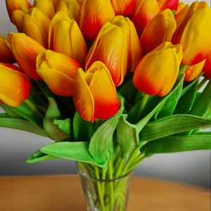 Peut inclure: Un bouquet de tulipes jaunes et orange avec des tiges vertes dans un vase en verre transparent.