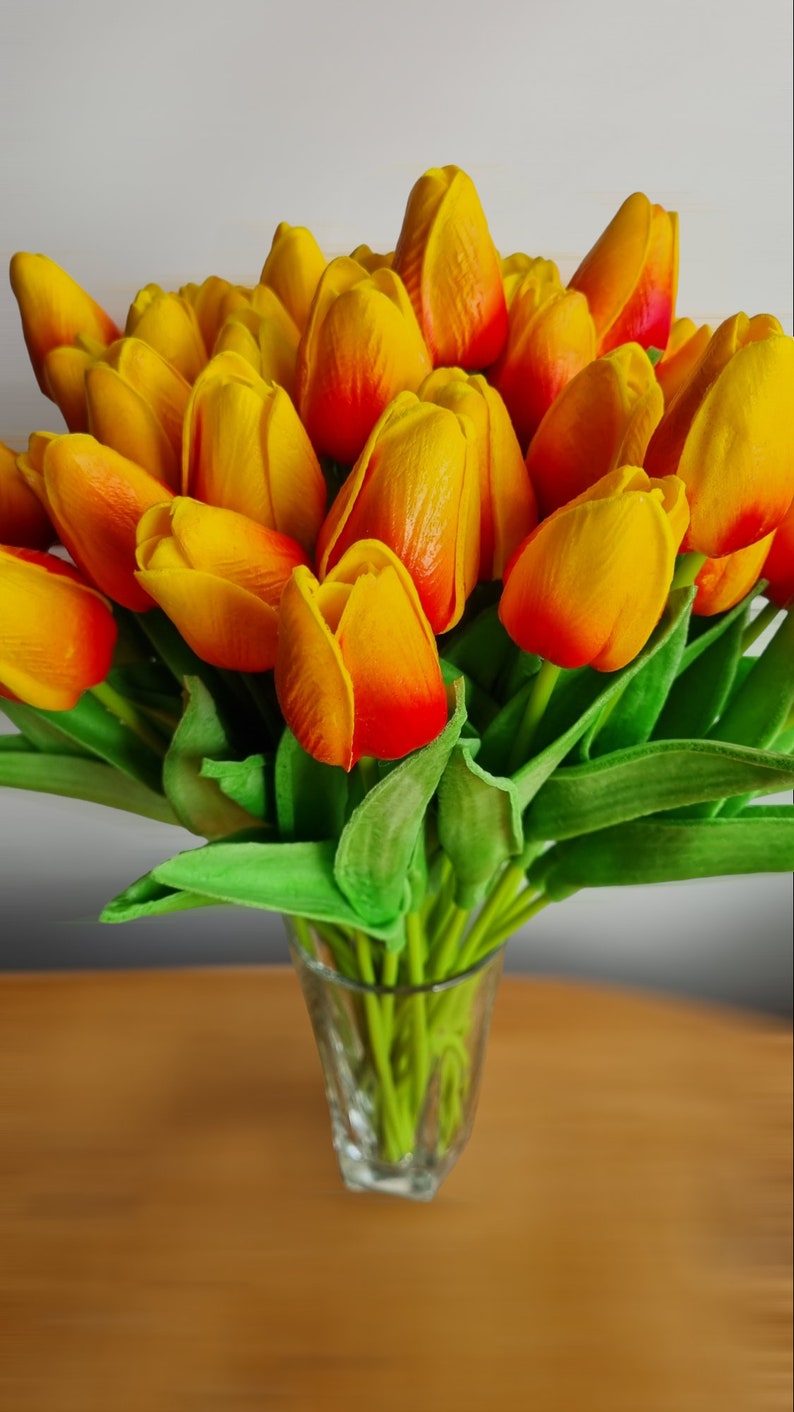 Peut inclure: Un bouquet de tulipes jaunes et orange avec des tiges vertes dans un vase en verre transparent.