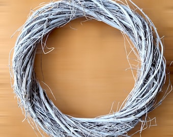 May include: A white twig wreath on a brown wooden background. The wreath is made of thin, white twigs that are woven together to form a circle.