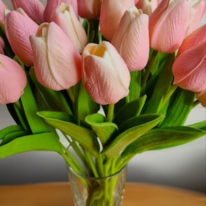 May include: A bouquet of pink tulips with green leaves in a clear glass vase.