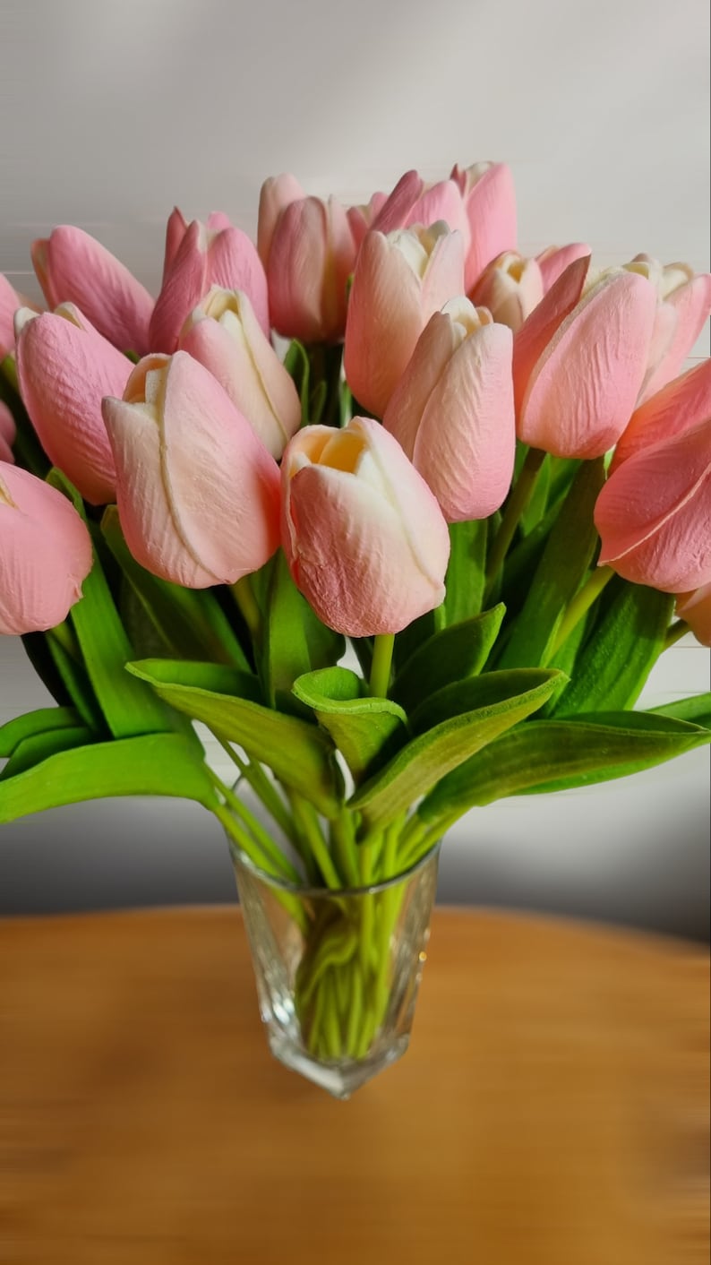 May include: A bouquet of pink tulips with green leaves in a clear glass vase.