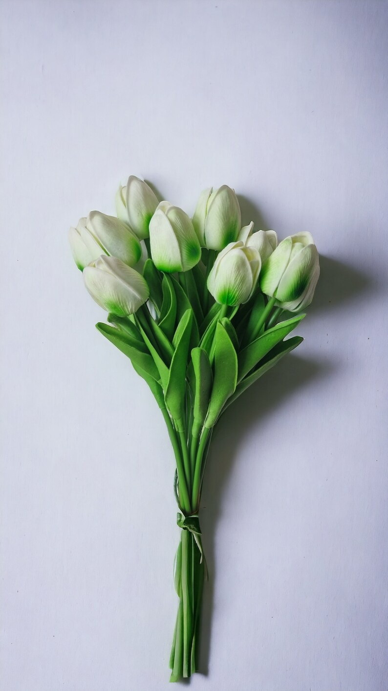 Peut inclure: Un bouquet de tulipes blanches avec des tiges et des feuilles vertes. Les tulipes sont li&eacute;es ensemble avec un ruban brun.