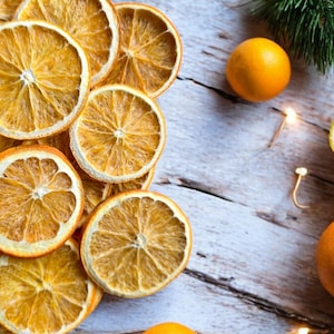 Puede incluir: Rodajas de naranja secas dispuestas en un patrón circular sobre una superficie de madera blanca. Las rodajas de naranja son de un color naranja vibrante y tienen un aspecto natural y rústico.
