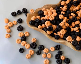 Puede incluir: Un cuenco de madera lleno de una gran colección de pequeños dulces con forma de calabaza en colores naranja y negro sólidos. Los dulces están esparcidos tanto dentro del cuenco como sobre la superficie, con crestas detalladas y forma redondeada.