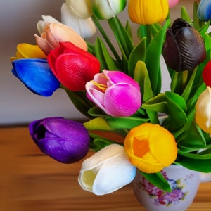 Puede incluir: Un ramo de tulipanes artificiales de colores en un jarr&oacute;n de cer&aacute;mica con estampado floral. Los tulipanes son en tonos de rojo, rosa, amarillo, azul, morado, blanco y negro.