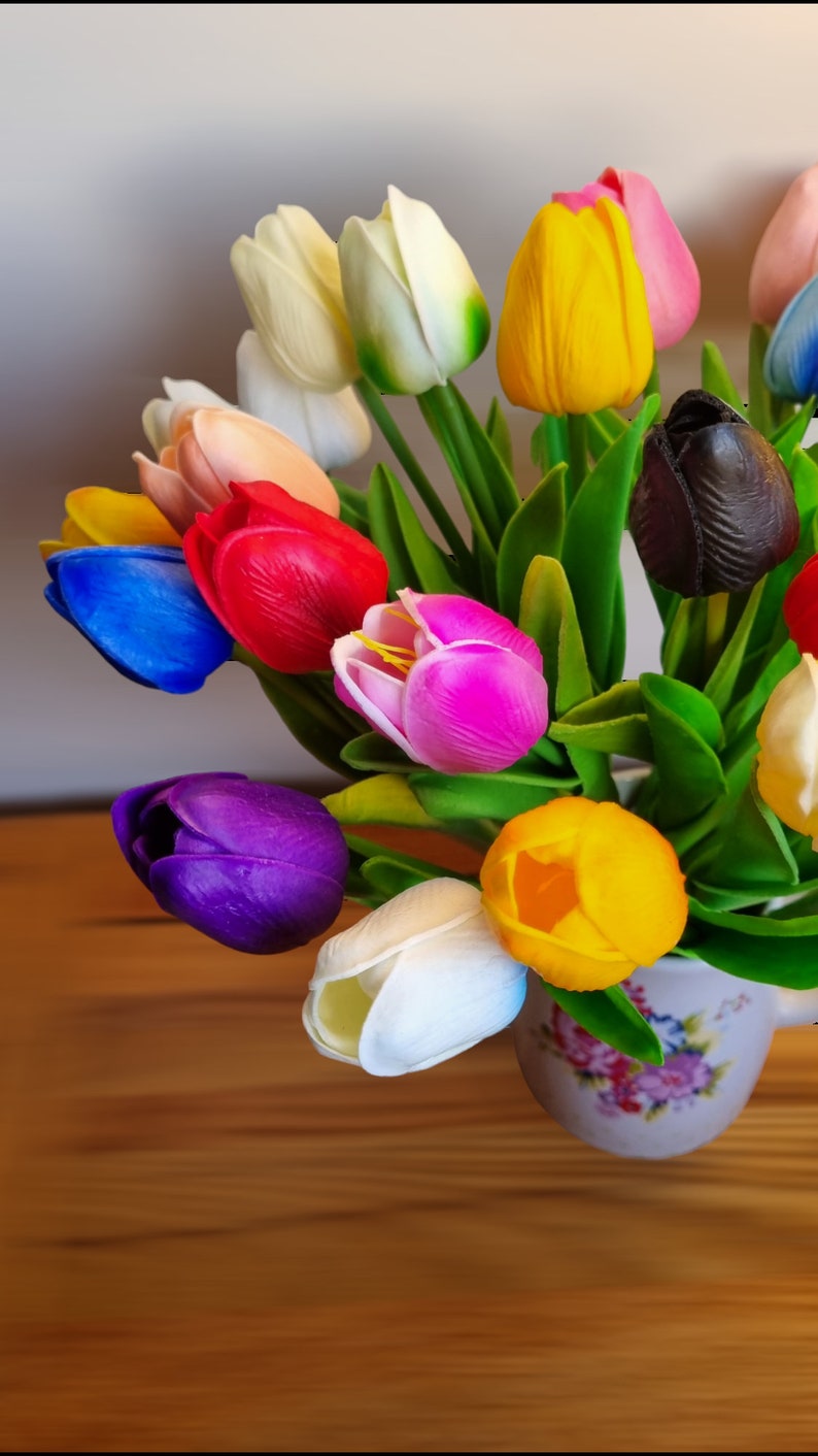 Puede incluir: Un ramo de tulipanes artificiales de colores en un jarr&oacute;n de cer&aacute;mica con estampado floral. Los tulipanes son en tonos de rojo, rosa, amarillo, azul, morado, blanco y negro.