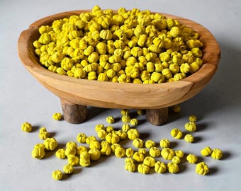 May include: A wooden bowl with three short legs filled with a large quantity of small, bright yellow, pumpkin-shaped decorative items. Several of these yellow, ribbed, spherical objects are scattered on the surface around the base of the bowl.