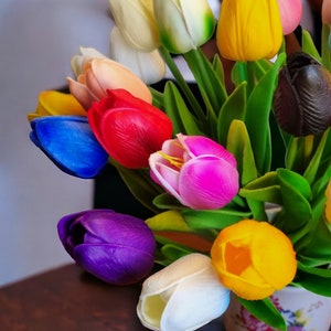 May include: A bouquet of colorful artificial tulips in a white ceramic vase with a floral pattern. The tulips are in shades of red, pink, yellow, blue, purple, and white.