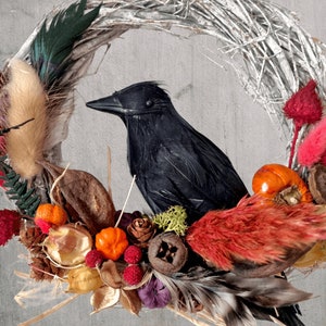Peut inclure: Un corbeau noir perch&eacute; sur une couronne de brindilles d&eacute;cor&eacute;e de fleurs s&eacute;ch&eacute;es, de baies et de plumes. La couronne est faite de mat&eacute;riaux naturels et a un aspect rustique. Le texte "Fluff & Co" est visible en bas de l'image.