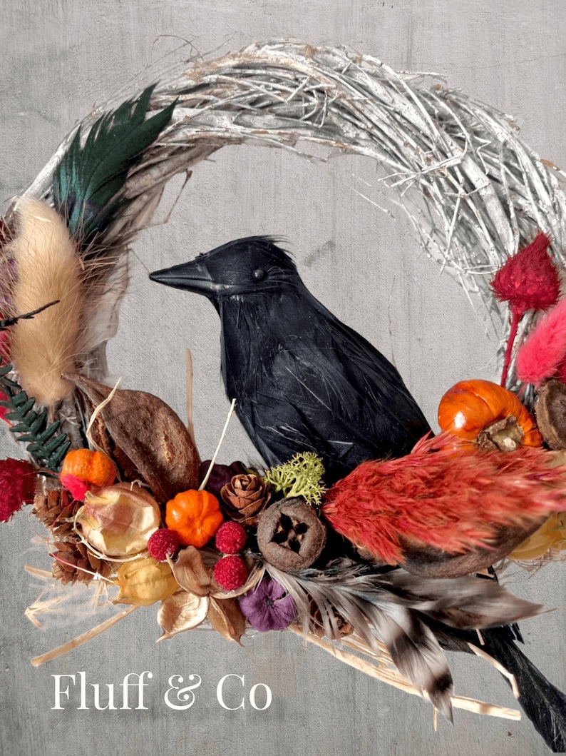 Peut inclure: Un corbeau noir perch&eacute; sur une couronne de brindilles d&eacute;cor&eacute;e de fleurs s&eacute;ch&eacute;es, de baies et de plumes. La couronne est faite de mat&eacute;riaux naturels et a un aspect rustique. Le texte "Fluff & Co" est visible en bas de l'image.