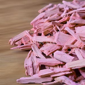 Puede incluir: Un montón de virutas de madera de color rosa. Las virutas son largas y delgadas, y están dispuestas en un patrón aleatorio. Las virutas están sobre una superficie de madera.