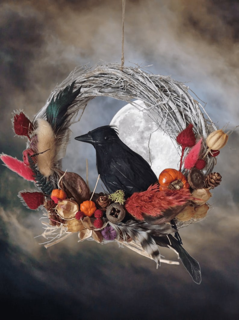 Peut inclure: Un corbeau noir perch&eacute; sur une couronne de brindilles d&eacute;cor&eacute;e de fleurs s&eacute;ch&eacute;es, de baies et de plumes. La couronne est suspendue &agrave; une ficelle et a une pleine lune en arri&egrave;re-plan.