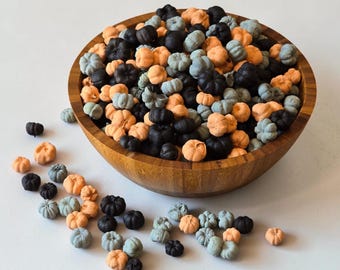 Puede incluir: Un cuenco de madera grande lleno de una colección de pequeñas decoraciones con forma de calabaza en tonos naranja, negro y azul grisáceo apagado. Varias decoraciones de calabaza en miniatura adicionales están esparcidas fuera del cuenco.