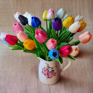Puede incluir: Un ramo de tulipanes artificiales de colores en una jarra blanca con un patr&oacute;n floral. Los tulipanes son en tonos de rosa, morado, azul, amarillo, blanco y naranja.
