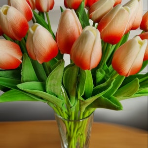 Peut inclure: Un bouquet de tulipes artificielles dans un vase en verre transparent. Les tulipes sont un m&eacute;lange de blanc et d'orange avec un effet d&eacute;grad&eacute;. Les tiges sont vertes.