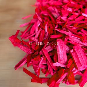 Peut inclure: Un tas de copeaux de bois rose vif. Les copeaux sont longs et fins, et ils sont disposés de manière aléatoire. Les copeaux sont sur une surface brun clair. © FLUFF & CO