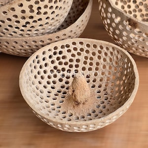 Peut inclure: Ensemble de quatre bols en osier naturel de forme circulaire avec un centre surélevé. Les bols sont faits d'un matériau brun clair et présentent un motif délicat et complexe de trous.