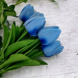 Puede incluir: Un ramo de tulipanes azules con tallos y hojas verdes sobre un fondo de madera blanca.