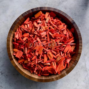 Puede incluir: Un cuenco de madera lleno de virutas de madera de color naranja brillante. Las virutas son pequeñas e irregulares en forma, y están dispuestas en un patrón aleatorio. El cuenco está hecho de madera oscura y tiene un acabado liso y pulido.