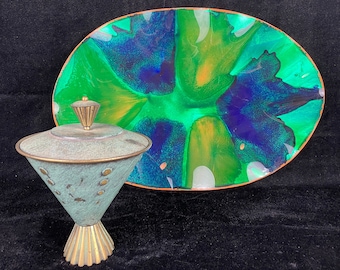 Può includere: Un vassoio ovale da portata verde e blu con un bordo in rame e una ciotola in metallo verde e oro abbinata con coperchio.