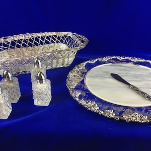 May include: A silver serving tray with a marble insert and a silver knife. There are four small glass salt and pepper shakers and a silver wire basket.