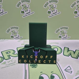 May include: A green and yellow stand with the words "Kickoff Collects" printed on it. A green figure of a football player is standing on the stand. The stand is surrounded by green and white cartoon characters.
