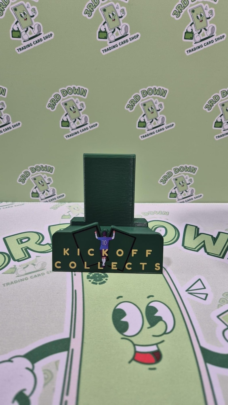 May include: A green and yellow stand with the words "Kickoff Collects" printed on it. A green figure of a football player is standing on the stand. The stand is surrounded by green and white cartoon characters.