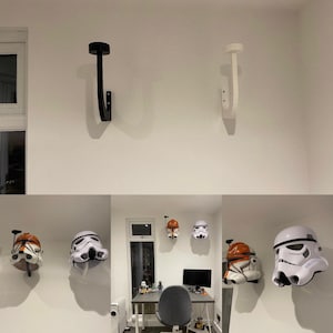 Op de afbeelding: Twee witte wandhaken met een zwarte haak aan de linkerkant. Er hangen vijf Star Wars-helmen aan de haken. De helmen zijn wit met oranje en zwarte accenten.