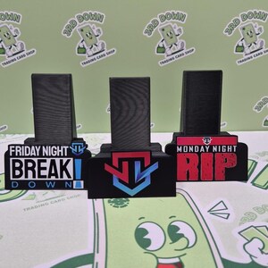 May include: Three black acrylic display stands with different designs. The first stand has a black and white graphic of a video game character with the text "Friday Night Break Down". The second stand has a blue, red, and white graphic of a video game character. The third stand has a red and white graphic of a video game character with the text "Monday Night Rip".