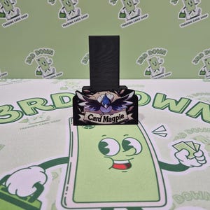 May include: A black wooden stand with a colorful graphic of a bird with the text "Card Magpie" on it.