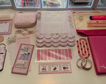 May include: A collection of pink and floral stationery items including a pencil case, a notebook, sticky notes, bookmarks, washi tape, and pens. The items feature various patterns, including stripes, bows, and book illustrations, with text such as Book Review and The Book Lover.