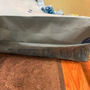 Puede incluir: Una bolsa de tela azul claro con las palabras "GO IN" y "GET" impresas en la parte inferior. La bolsa tiene una correa amarilla y azul.