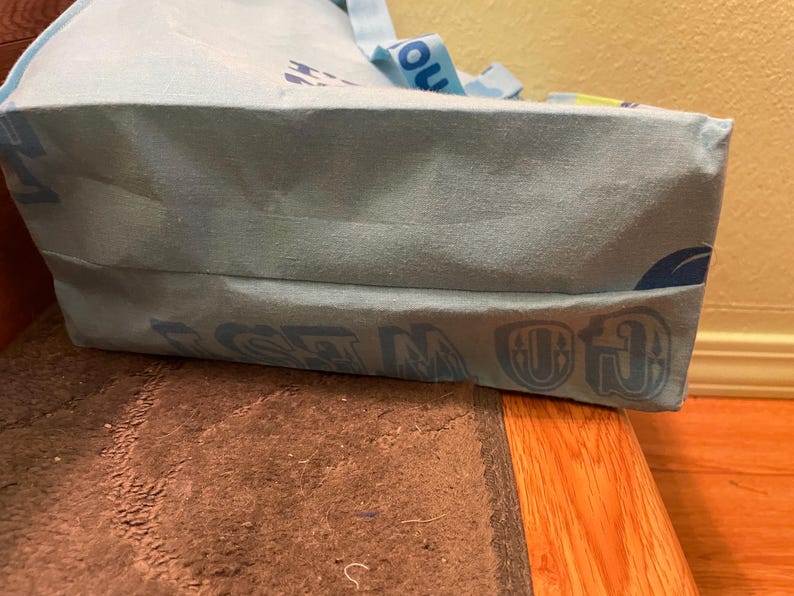 Puede incluir: Una bolsa de tela azul claro con las palabras "GO IN" y "GET" impresas en la parte inferior. La bolsa tiene una correa amarilla y azul.